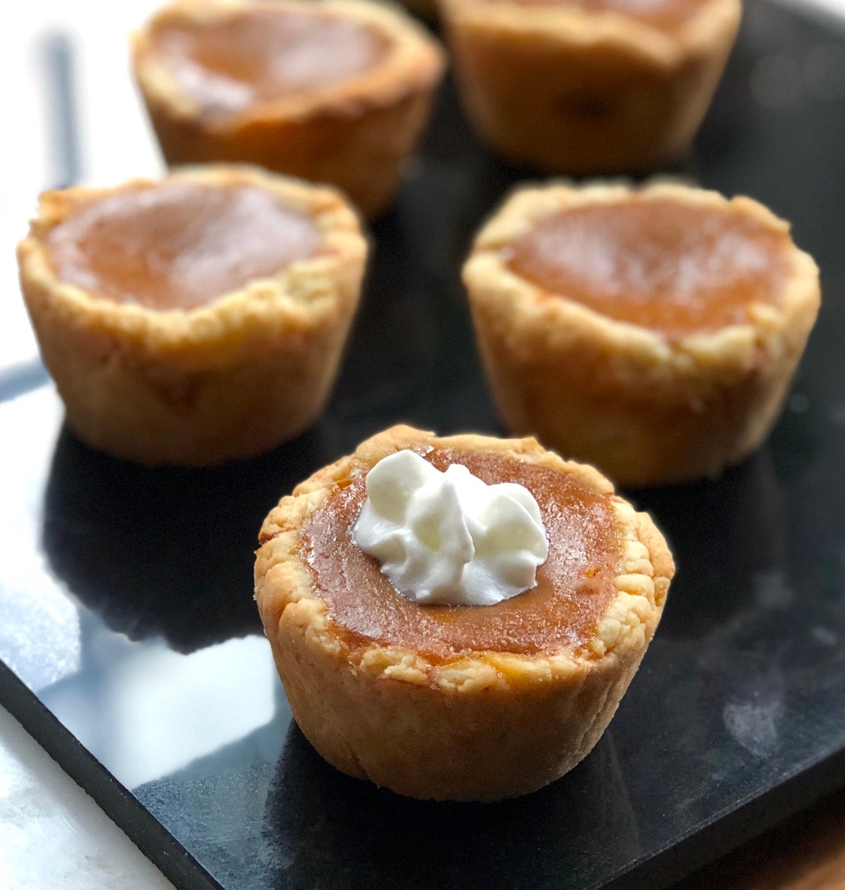 Mini pumpkin pied on a piece of black marble, one topped with whipped cream.